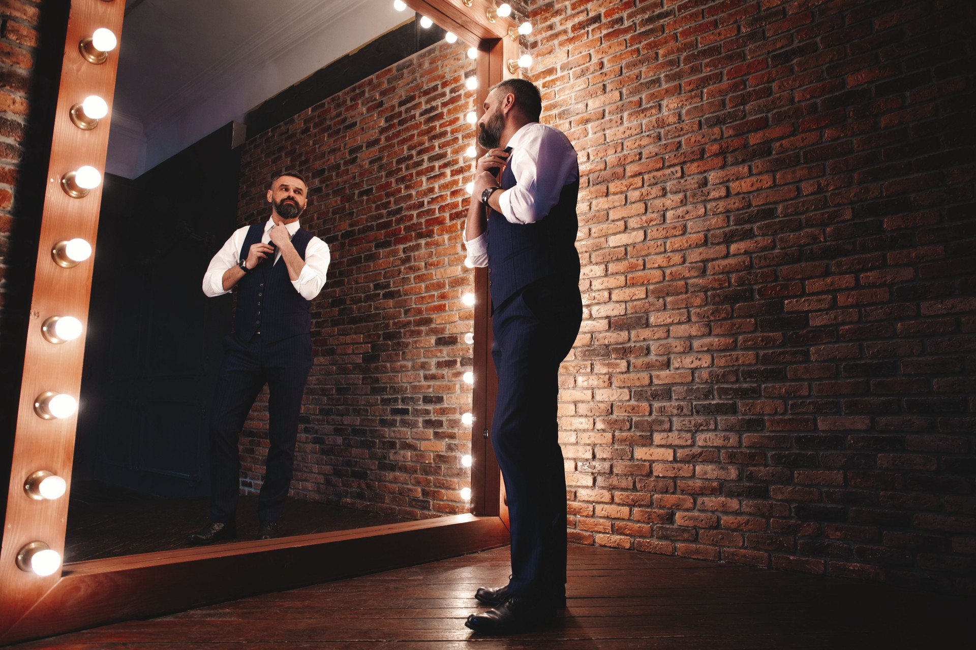 Look élégant. Pleine longueur de bel homme en costume complet ajustant sa veste tout en se tenant devant le miroir à l’intérieur